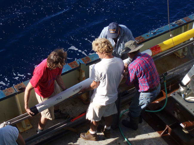 The core liner [full of stratified sediment] is received and cut into sections at the bottom of the core.