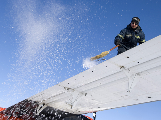 Travis Goetzinger sweeps the frost off of the wings of the Twin Otter in preparation for takeoff.