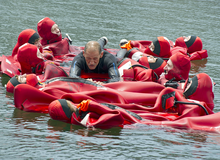 ten people in survival suits form a raft to support an unsuited person