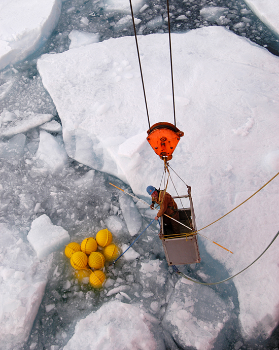 John Kemp is lowered by the ship's crane to hook a group of floats