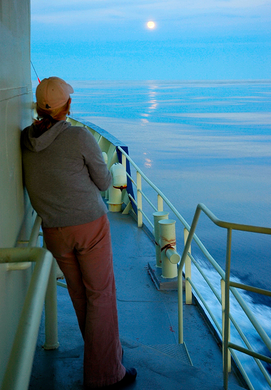 Messman Kathryn Eident, looks at the moon in the distance from the deck of R/V Oceanus.