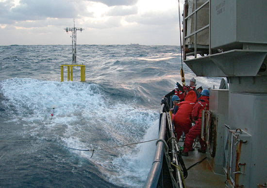 Researchers and crew members struggle to deploy a spar buoy in rough seas.