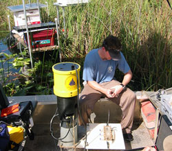 Research Assistant Matt Allen sits on an airboat and sets up a WHOI-designed automated seepage meter for a three-week deployment in the Florida Everglades.
