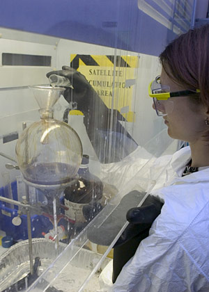 Emma Teuten pours concentrated sulfuric acid into flask full of fat-filled whale extract, turning the mixture black.