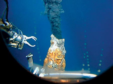 Alvin's manipulator reaches toward a black smoker chimney, seen through the sub's viewport, at 17 degrees S on the East Pacific Rise.