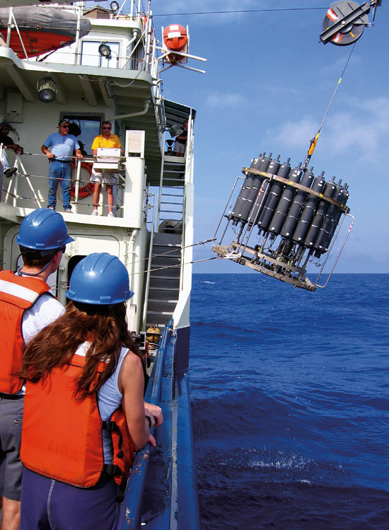 R/V Oceanusc Bosun Jim MGill (top, blue shirt) and Able Seaman Bill Hoff (yellow shirt) operate the winch to deploy a conductivity-temperature-depth (CTD) water sampler into the Sargasso Sea, as WHOI oceanographer Dennis McGillicuddy (bottom left) and Rutgers University Postdoctoral Scholar Diana Nemergut look on.