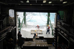 Ocean Technology Group technicians Justin Smith and Paul Balch work to secure the Bongo net on the aft deck while a group watches from the safety of the hangar.