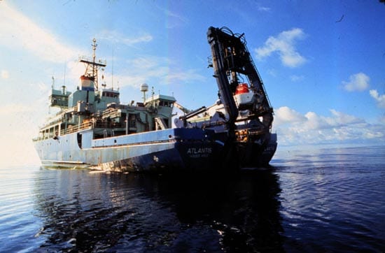 R/V Atlantis prepares to launch Alvin. The submarine and its red hatch cover are visible at the stern, hanging beneath an A-frame winch. (Woods Hole Oceanographic Institution)