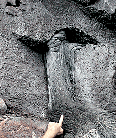 A finger pointing to the lava flow that has traveled through the small lava tube in the cliff face. Scale across photo is about 1 meter.