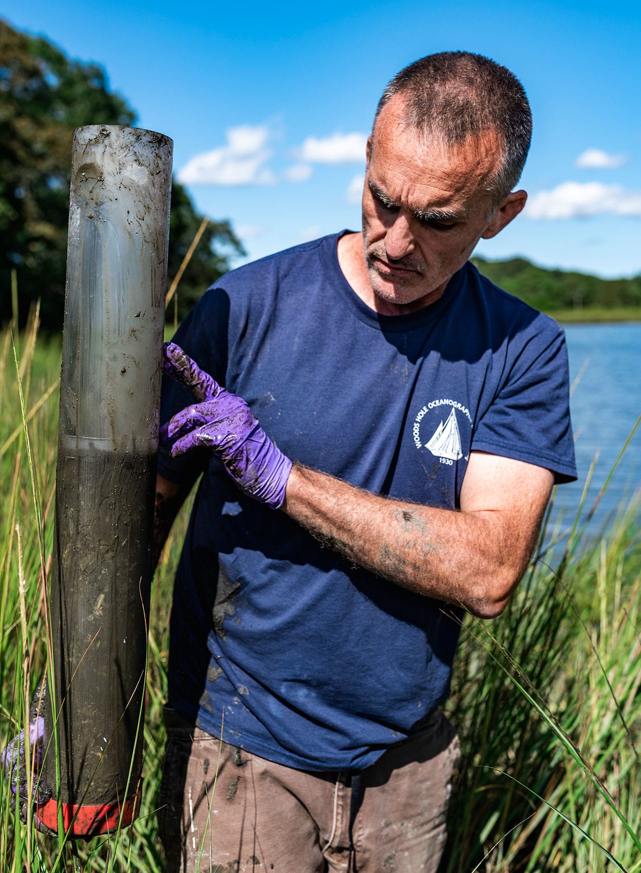 WHOI marine geochemist, Christopher Reddy, holds up a PVC pipe core of the sediment, something he calls a natural tape recorder for what happened to the land throughout the years. This includes the West Falmouth Oil Spill, which can be detected six inches deep in soil. (Photo by Daniel Hentz, Woods Hole Oceanographic Institution)