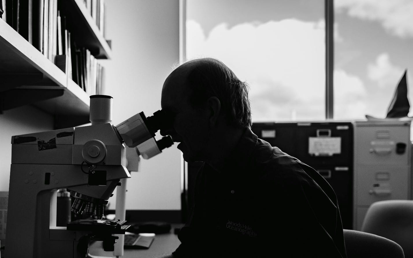 Biologist Michael Moore, director of the Marine Mammal Center at WHOI, sits at the microscope he has used for more than 30 years. (Photo by Daniel Hentz, WHOI)