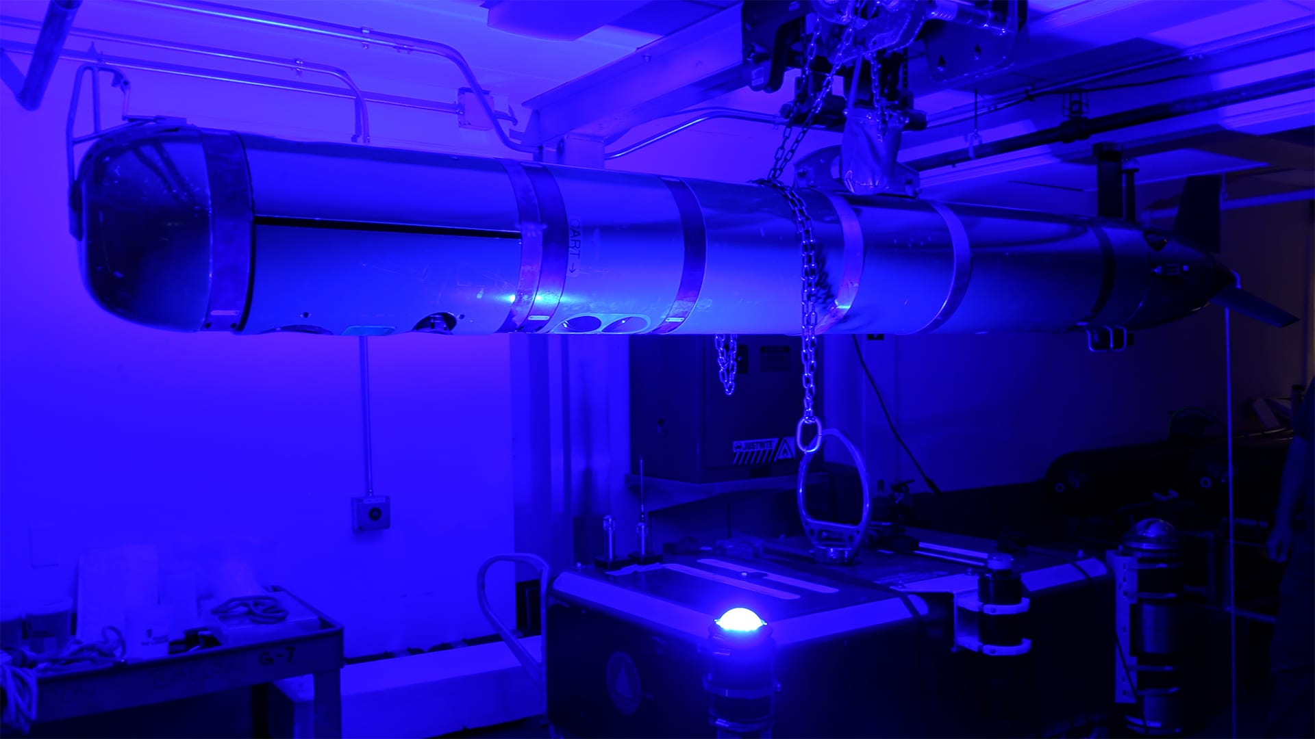 A REMUS-600 autonomous underwater vehicle (AUV) communicates with an ocean-bottom seismograph (OBS) via a WHOI-developed optical modem link during lab testing. This link enables REMUS vehicles to act as "seismic data mules" whereby they offload data OBS stations without the need for ships or human intervention. (Photo by Dara Tebo, © Woods Hole Oceanographic Institution)