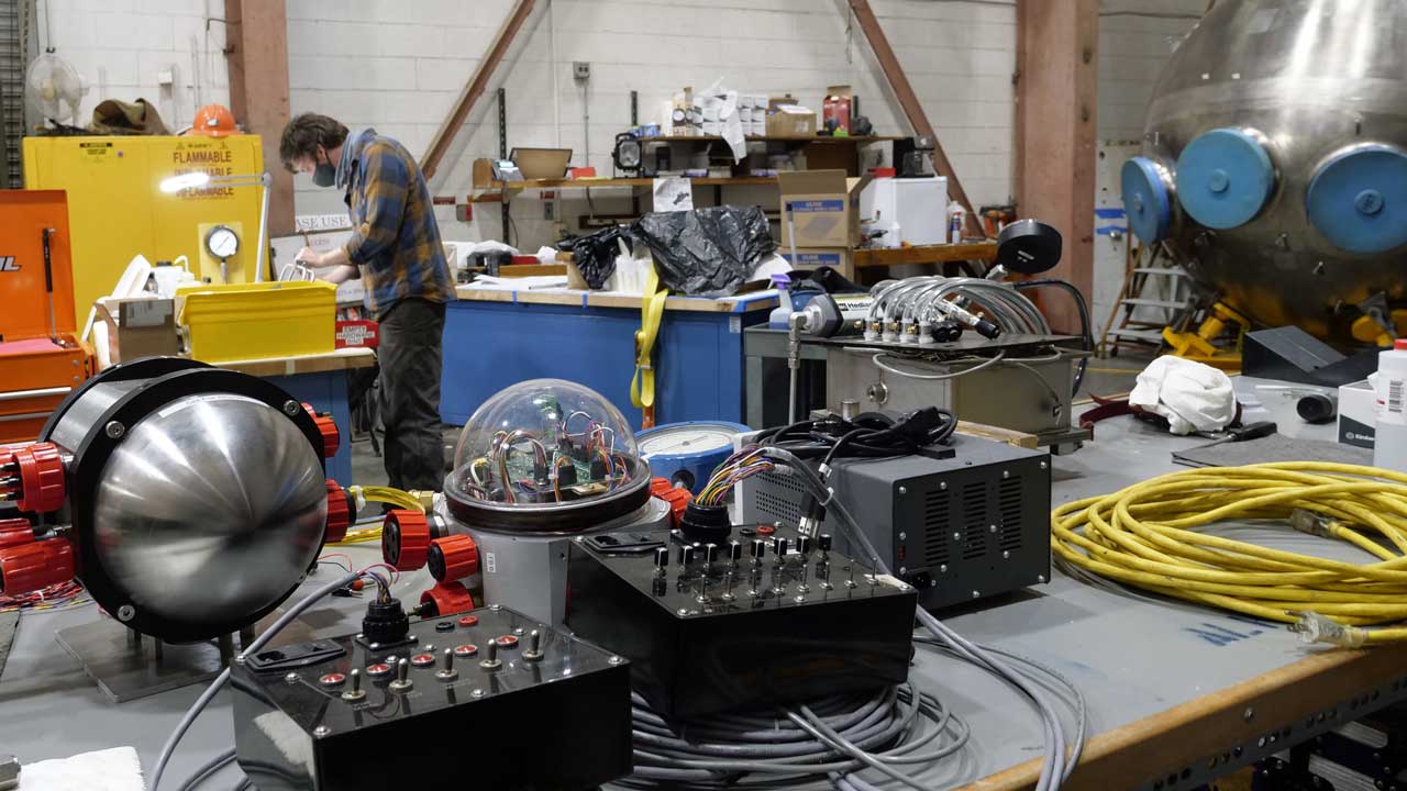 Danik Forsman in the WHOI High Bay working on the new variable ballast pump for Alvin. Sub sphere, right.