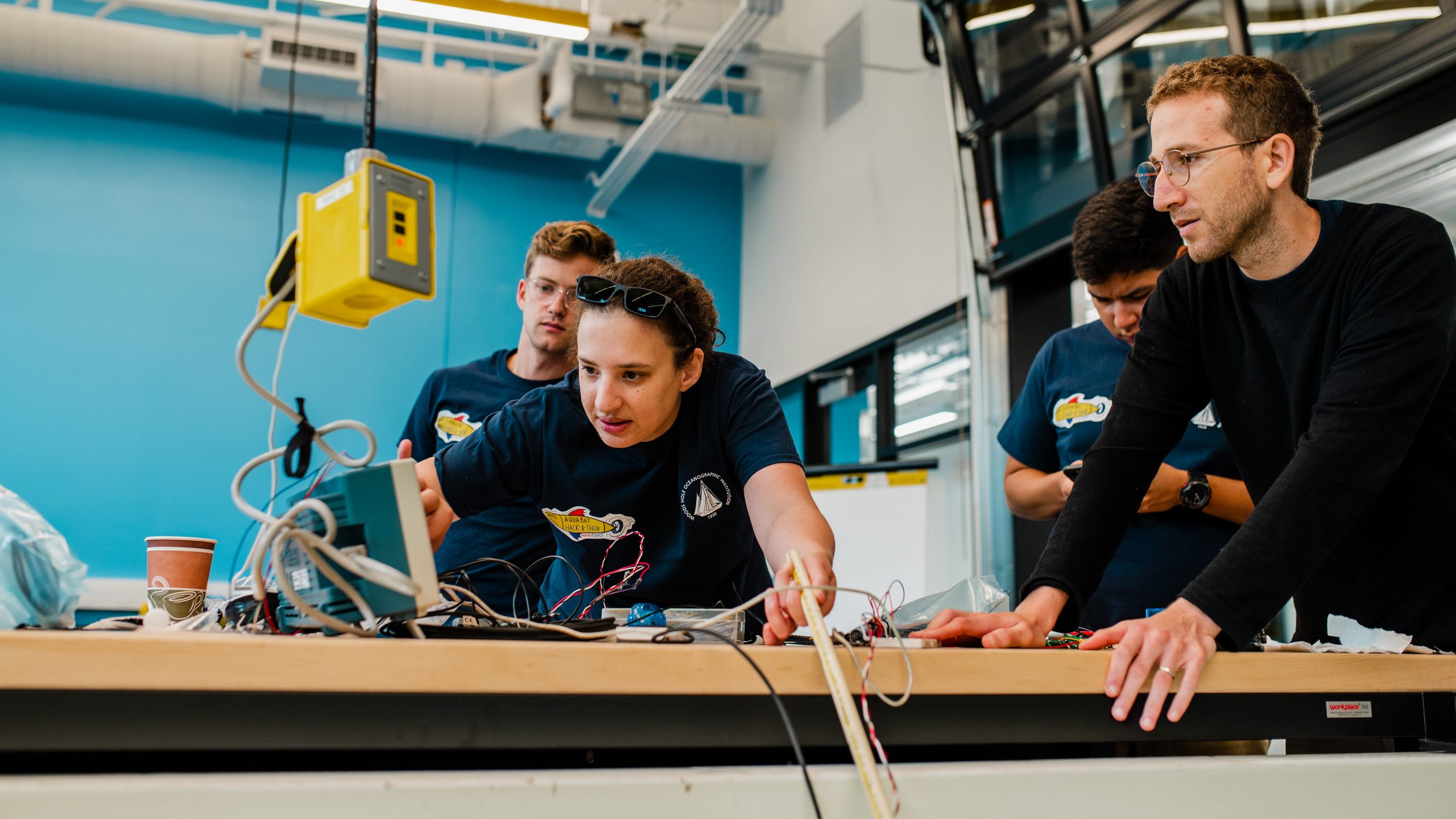 DSC_2528 WHOI assistant scientist and engineer Erin Fischell (center left) gathers with Ben Weiss (far left), MIT-WHOI Joint Program student Matthew Flores (center right) to assess whether a new "mechanical ear" acoustic sensor is working during the MURAL Hackathon. (Daniel Hentz, © Woods Hole Oceanographic Institution)