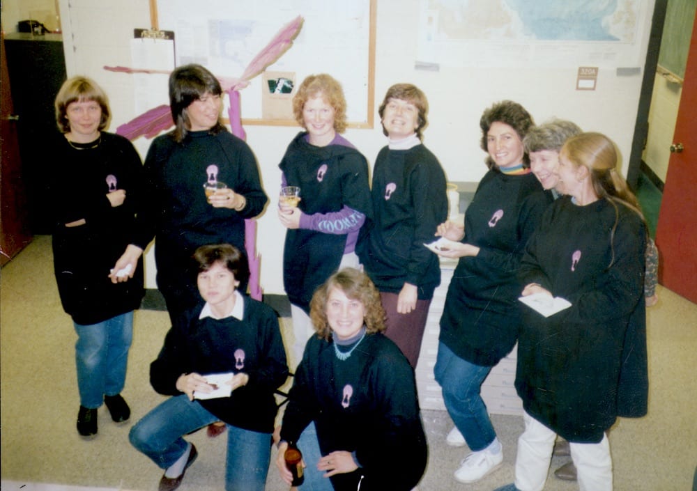 Nine women wearing Data Dolly shirts pose for a photo in the late 70s.