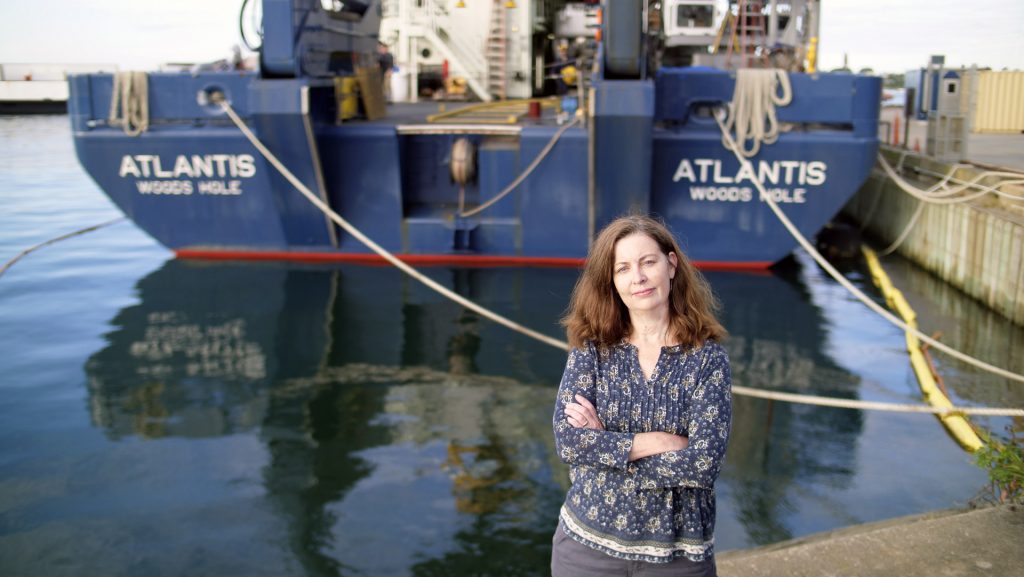 Alvin Certification Coordinator Lisa Smith standing in front of an updated HOV Alvin which is tucked on board the newly refurbished R/V Atlantis (Photo Ken Kostel ©WHOI).