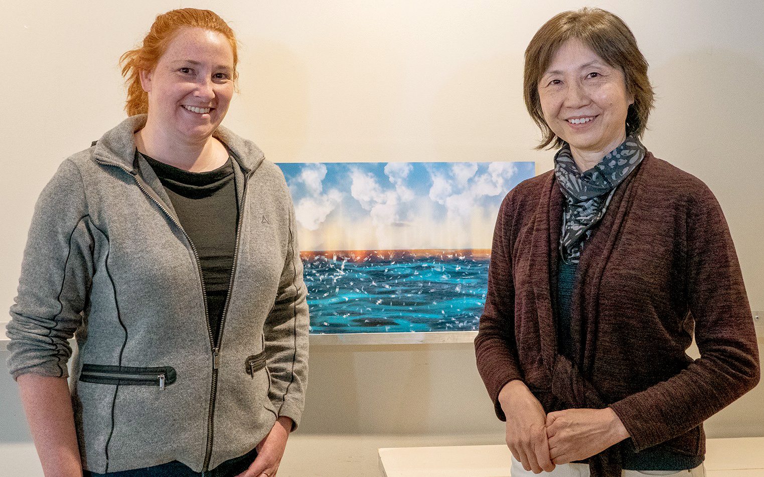 WHOI physical oceanographer Caroline Ummenhofer (left) and Rhode Island-based artist Hong Xu pose with Xu's painting "Surfacing Basic Elements" at a Falmouth Art Center exhibition in May 2021. (Photo by Ruth Clegg)