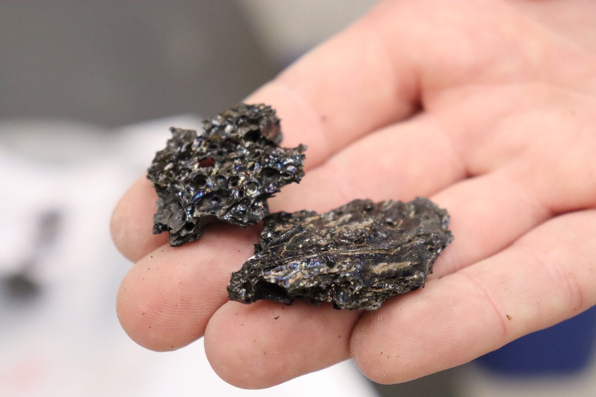 Horton holds pieces of tephra (cooled lava) collected from the 2018 eruption of Kilauea on the Big Island of Hawai’i. This lava was ejected into the air, where it quenched to shiny glass. (Photo by Elise Hugus, © Woods Hole Oceanographic Institution)