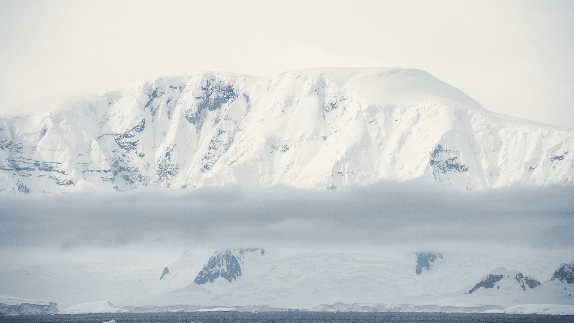 In Antarctica, a mountain peak receives snow from moving clouds in the distance. (Photo by Dan Lowenstein, © Woods Hole Oceanographic Institution)