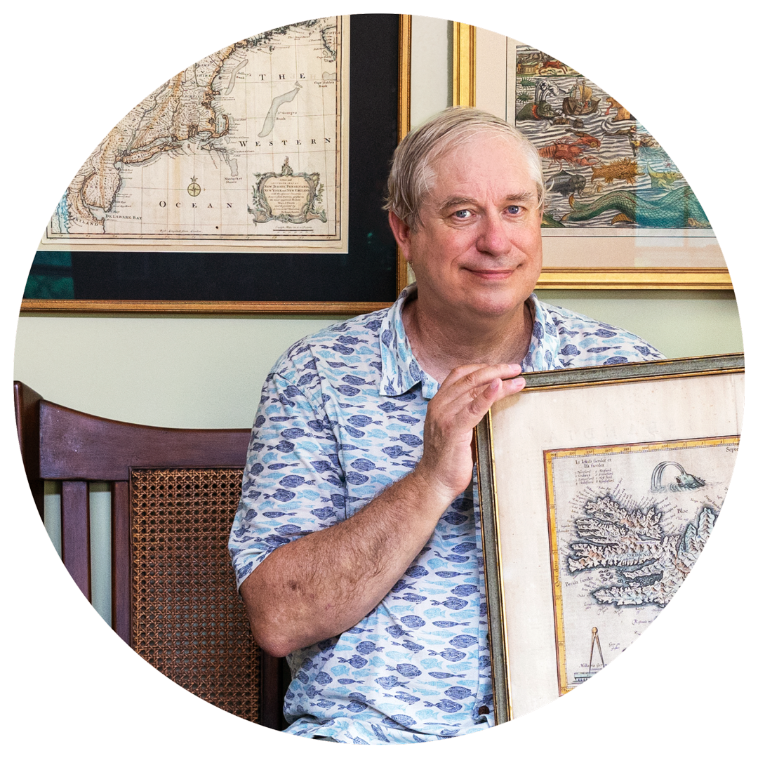 A man holding a map with several other maps on the wall behind him.