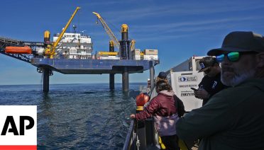 Expedition 501 members look down from the Liftboat Robert platform, to the approaching Gaspee, a crew transport vessel, in the North Atlantic, Saturday, July 19, 2025. (AP Photo/Carolyn Kaster)