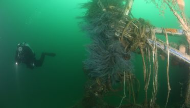 A diver swims near a wreck draped with lost fishing nets. (Photo courtesy of NOAA)