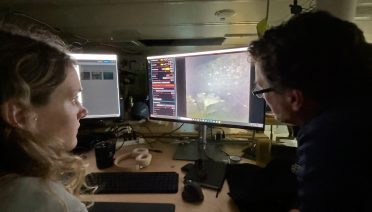 WHOI imaging specialists Dwight Coleman (right, also the Chief Scientist of the Heroic Age Expedition) and Zoe Daheron (left) watch as real-time images of the wreck of Sir Ernest Shackleton’s Quest are transmitted from the seafloor off the coast of Labrador and Newfoundland to a lab on the research vessel Atlantis. (Photo by Ken Kostel, © Woods Hole Oceanographic Institution)
