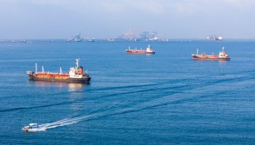 Cargo ships and tankers sitting at anchor outside a busy commercial port