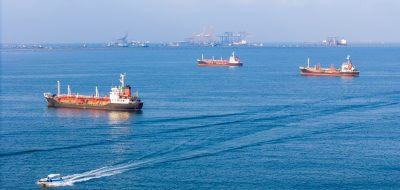 Cargo ships and tankers sitting at anchor outside a busy commercial port