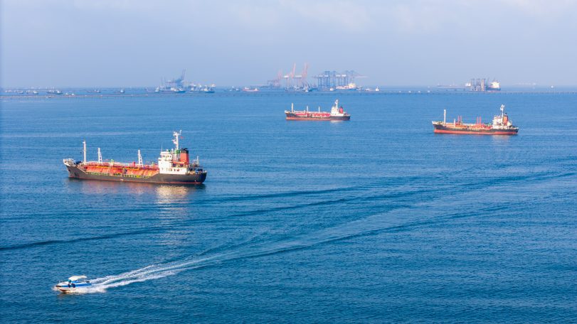 Cargo ships and tankers sitting at anchor outside a busy commercial port