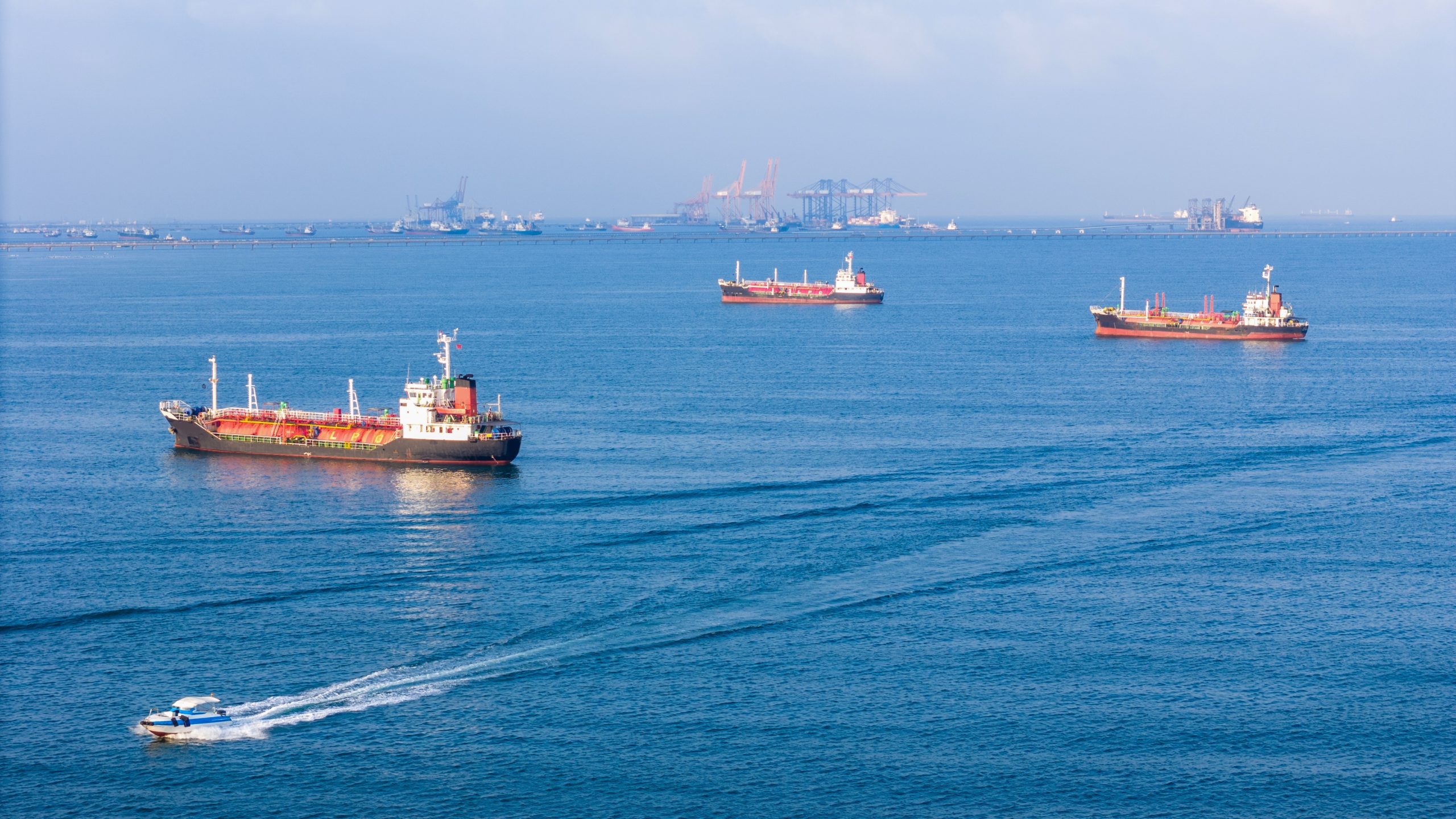 Cargo ships and tankers sitting at anchor outside a busy commercial port