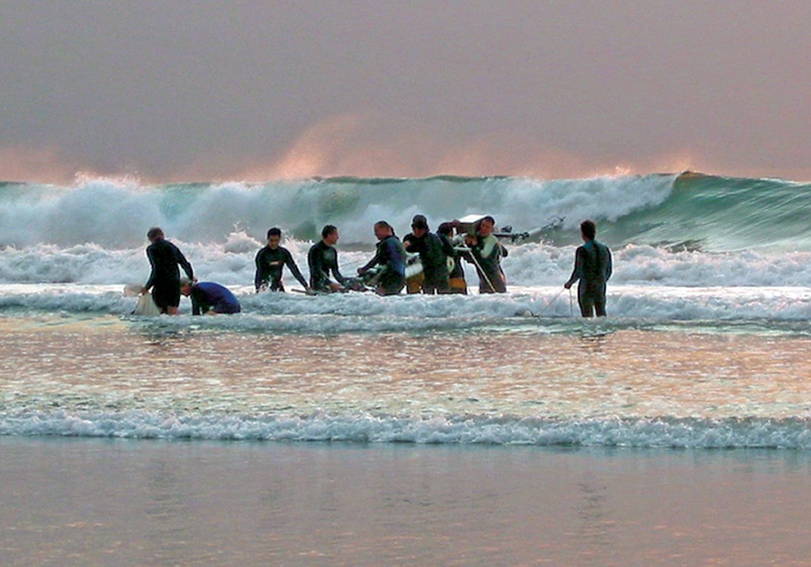 Researchers carry and instrument tower into the surf to measure the movement of water beneath the breaking waves.